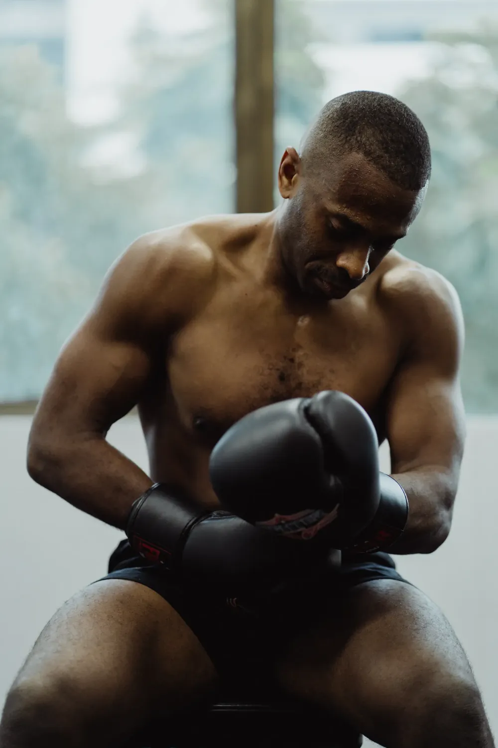 A boxer sitting quietly with his gloves on, head bowed, in the quiet moments before a fight