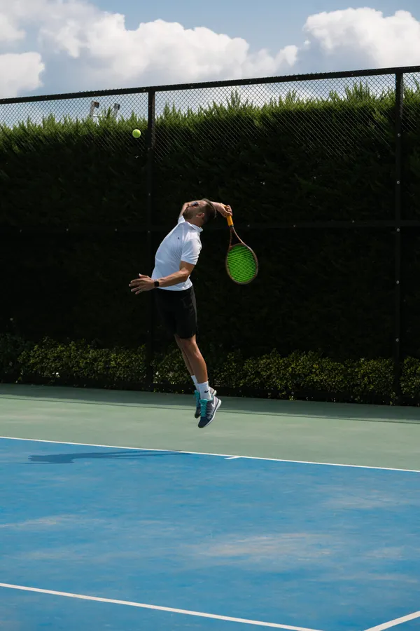 Tennis player leaping into a serve on an outdoor court